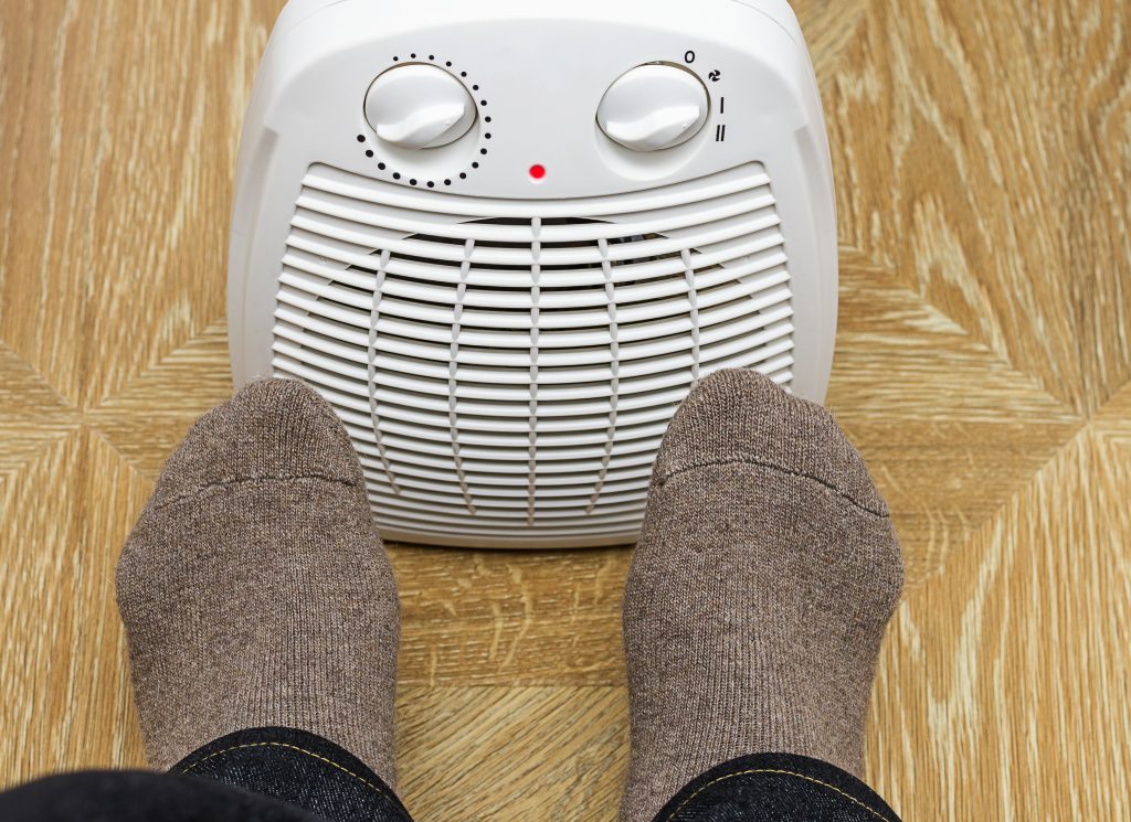 Man warming feet by front electric space heater.